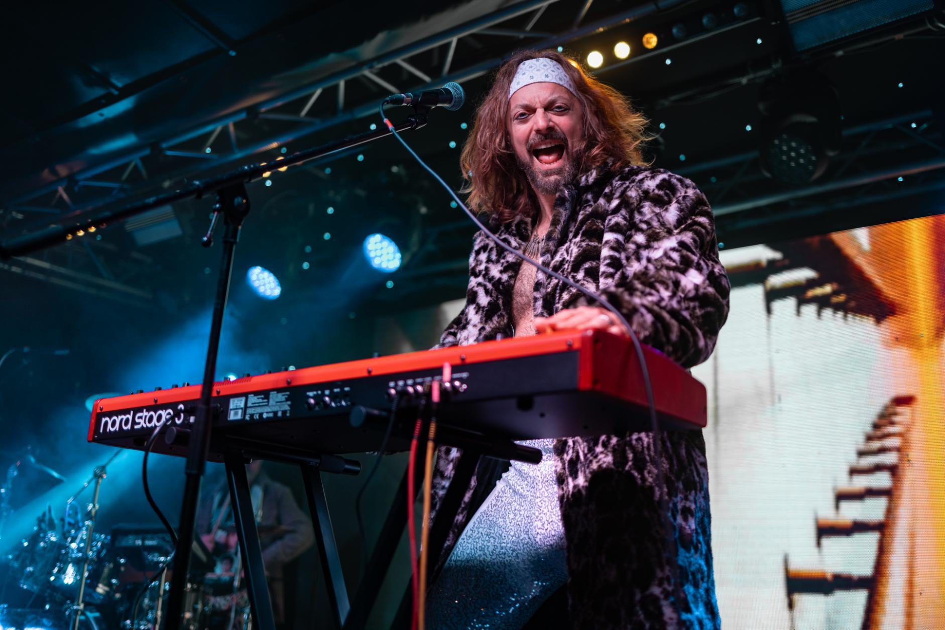 Man playing keyboard and singing with headband and long furry coat