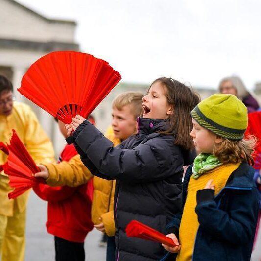 Group of young children holding big red fans for Chinese New Year workshop in Guildhall Square