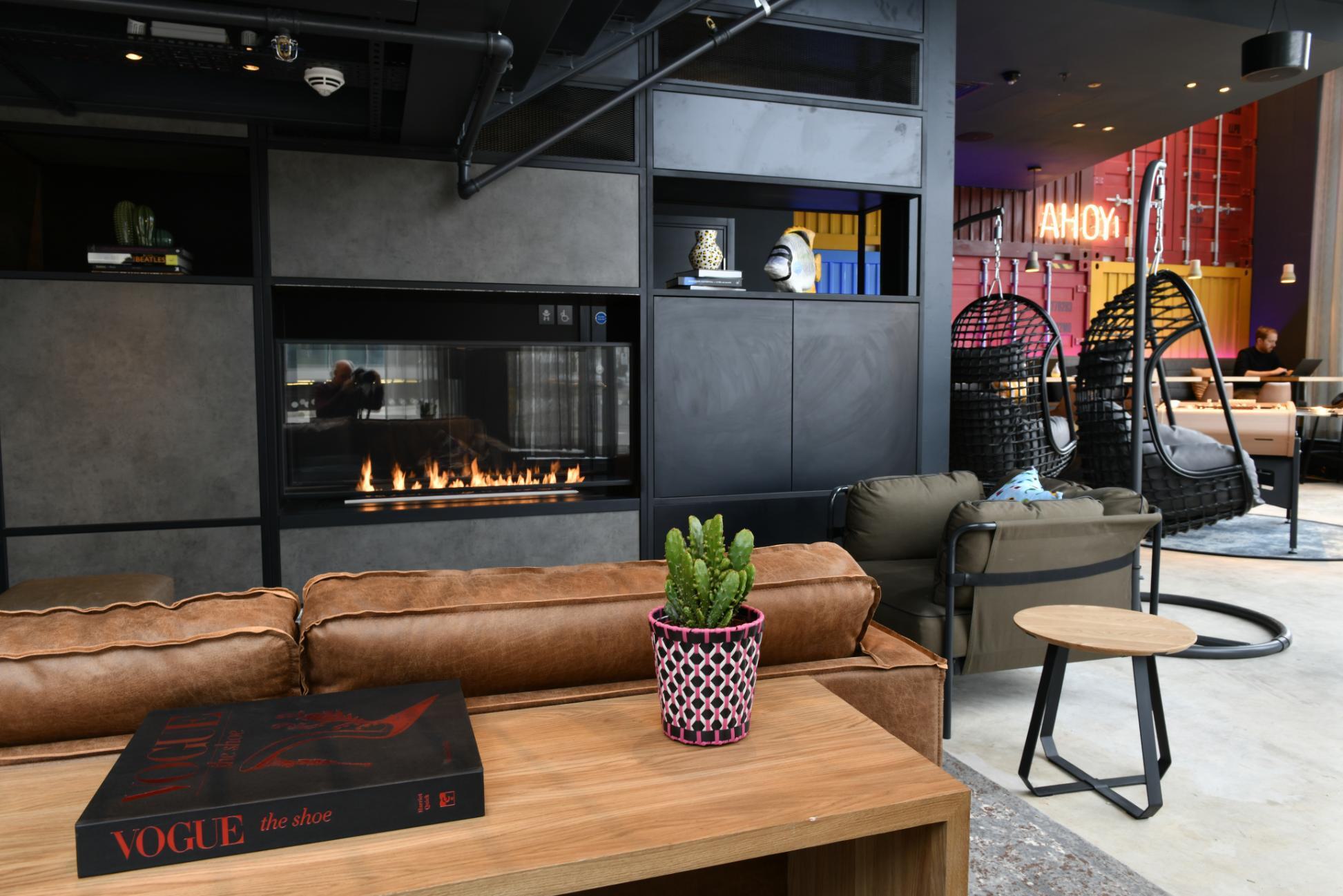 Modern communal living space with fireplace and hanging nest like chairs in Moxy Hotel