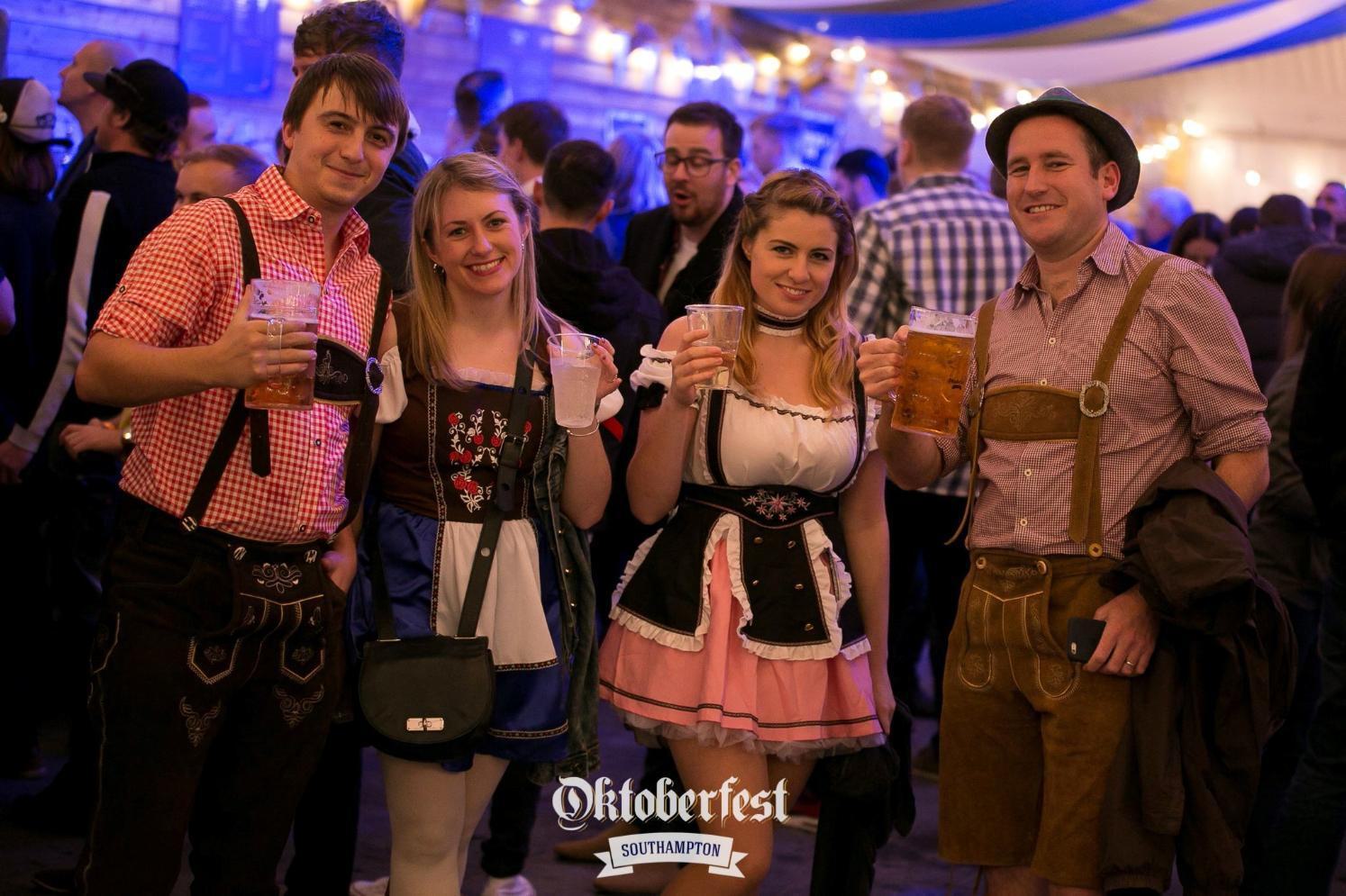Four people standing and smiling with drinks at Oktoberfest