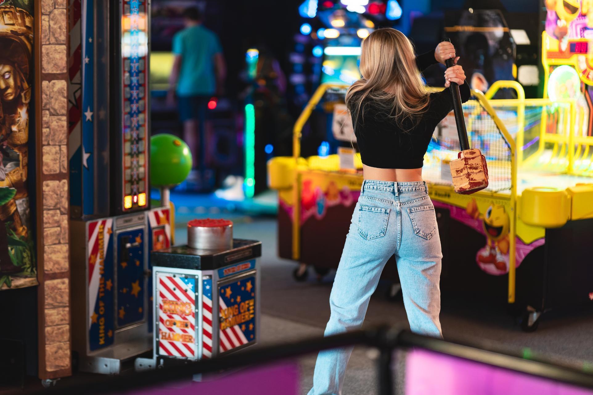 Young women with blonde hair swinging a hammer on a strength testing game at High Score Arcade