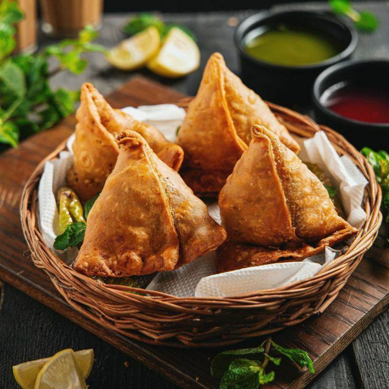 Four veggie samosas from Padharo in woven willow basket next to dipping sauces